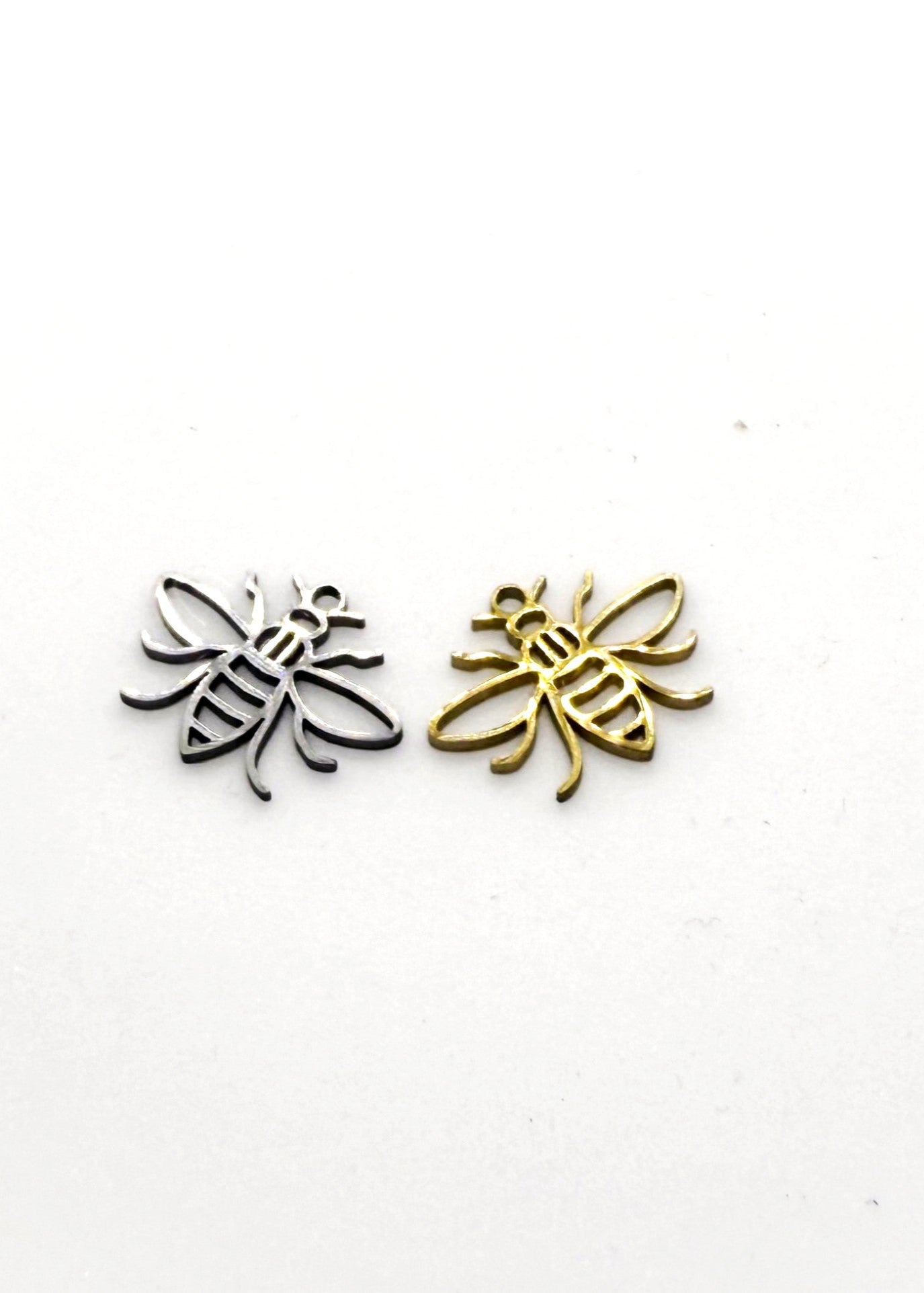 Two stainless steel bee-shaped charms, one gold and one silver, on a white background.
