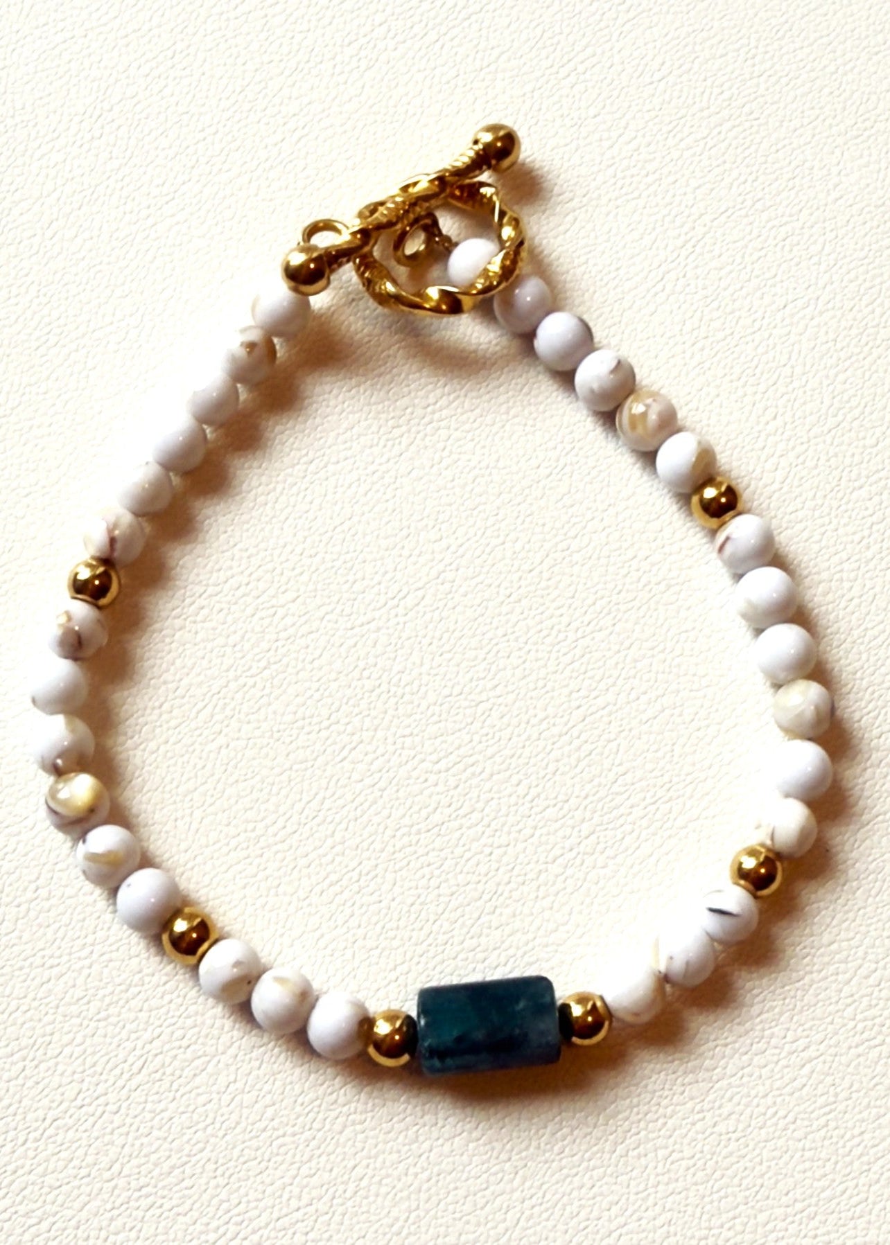 Beaded bracelet with white, gold, and blue beads on a light background